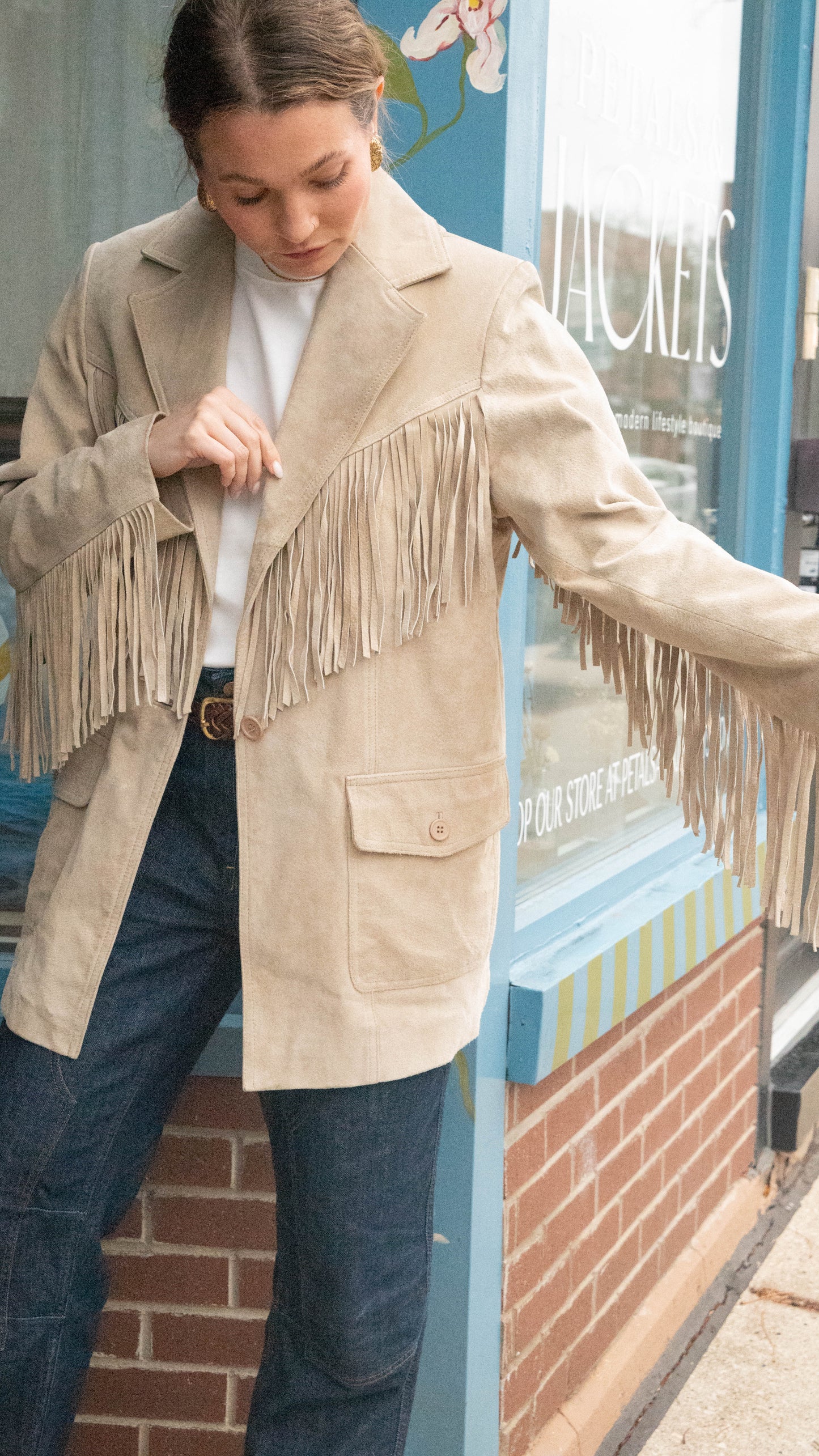 Woman poses in front of Chicago Vintage Boutique Petals & Jackets wearing a Vintage Fringe Western Jacket for fall showing off fringes on arms.