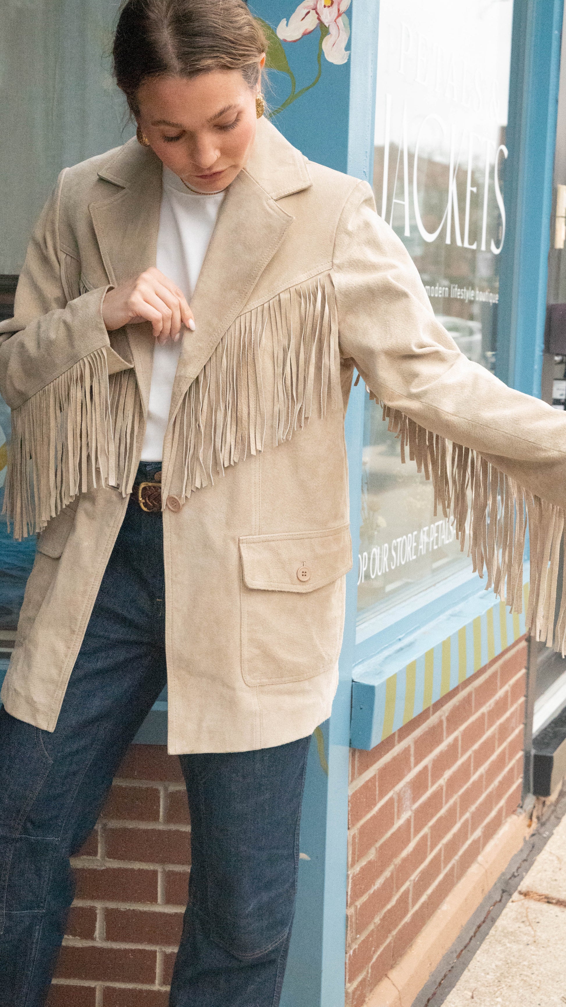 Woman poses in front of Chicago Vintage Boutique Petals & Jackets wearing a Vintage Fringe Western Jacket for fall showing off fringes on arms.