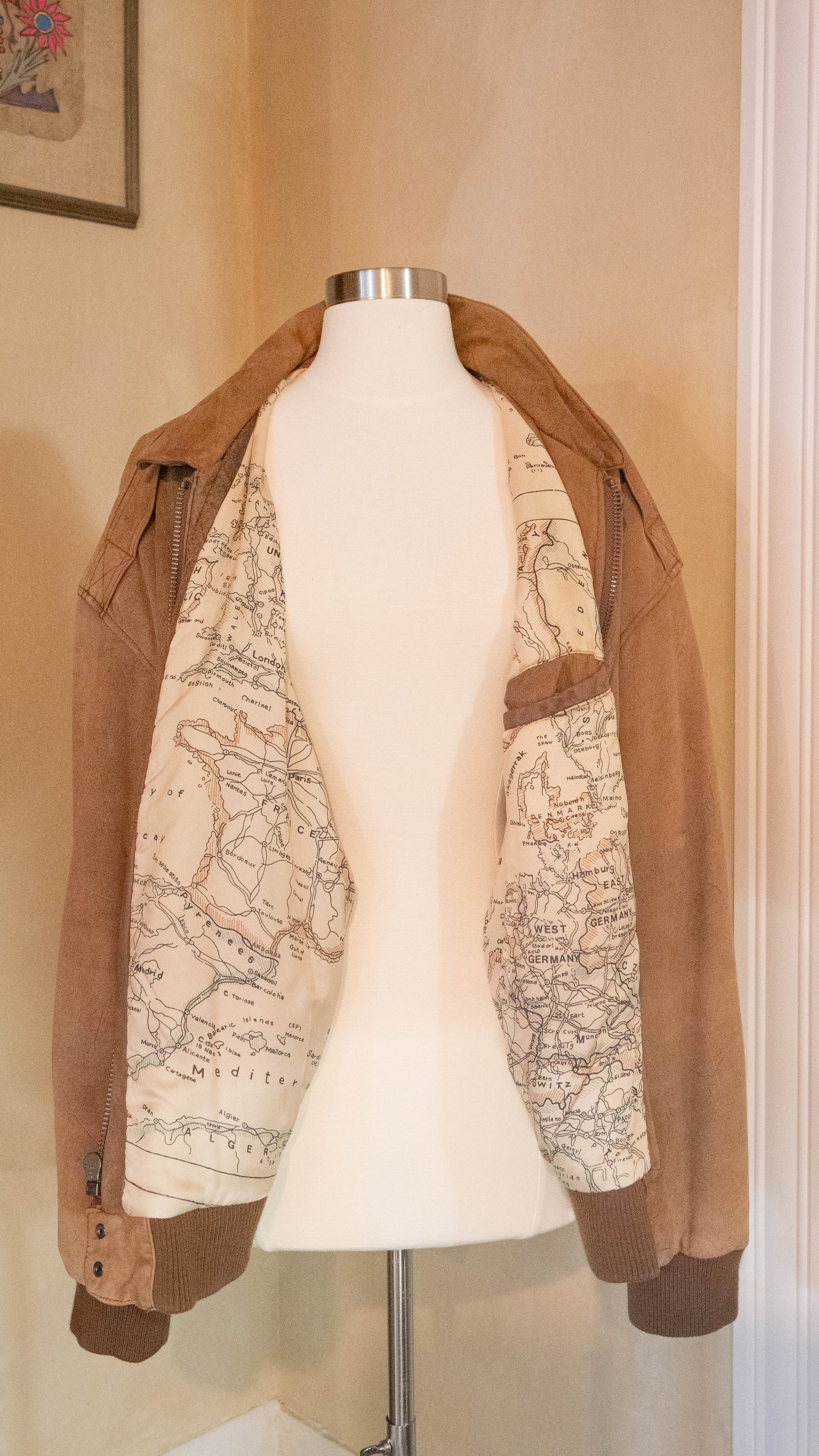 Vintage brown jacket with map lining on back of mannequin pictured in the corner of Petals and Jackets Boutique.