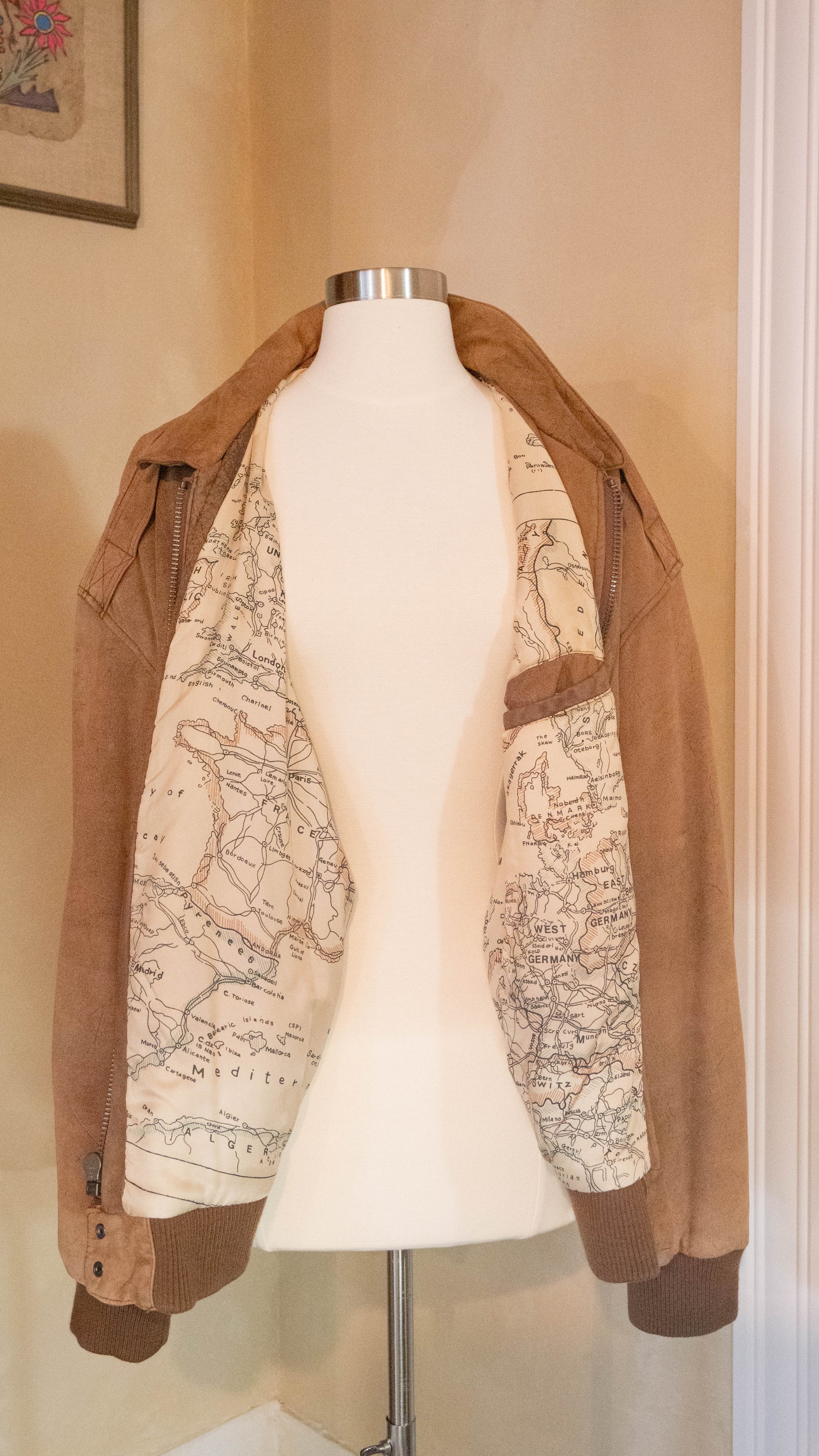 Vintage brown jacket with map lining on back of mannequin pictured in the corner of Petals and Jackets Boutique.