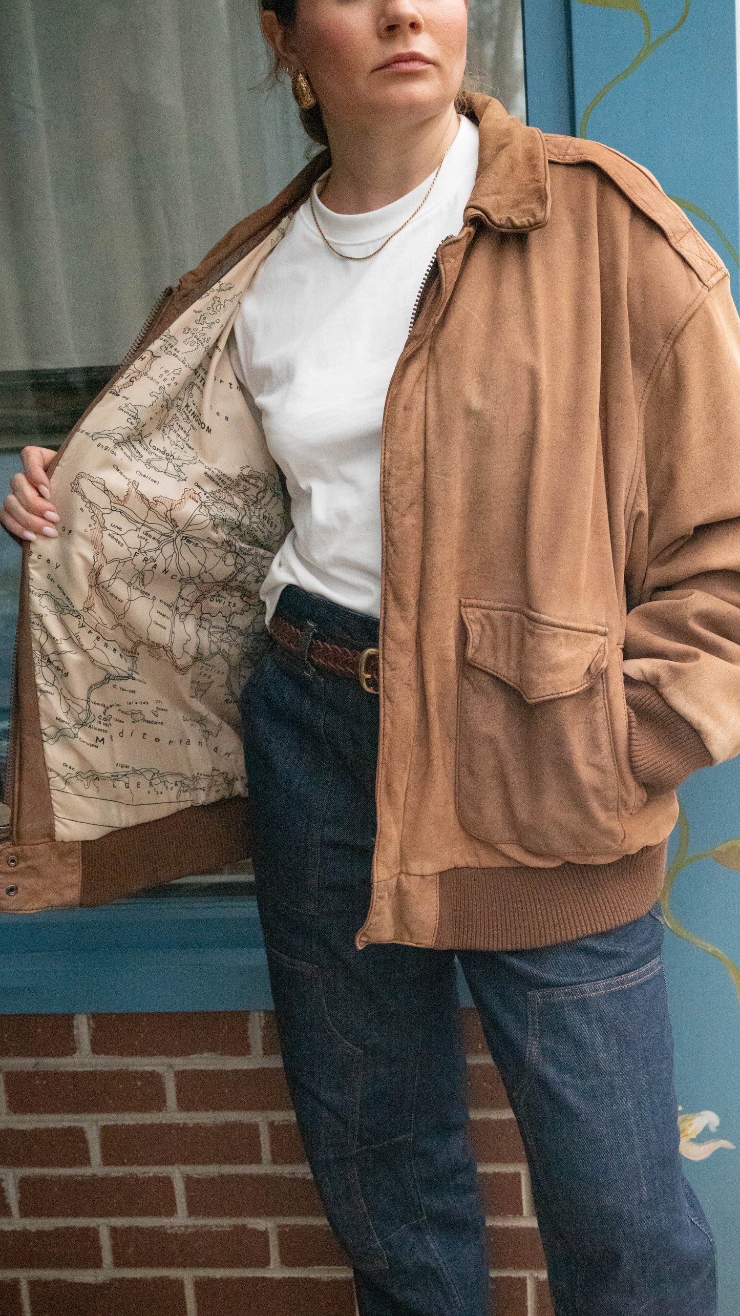Woman stands in front of a vintage boutique in Chicago, Illinois wearing a leather jacket with a photo of a vintage map in the lining.