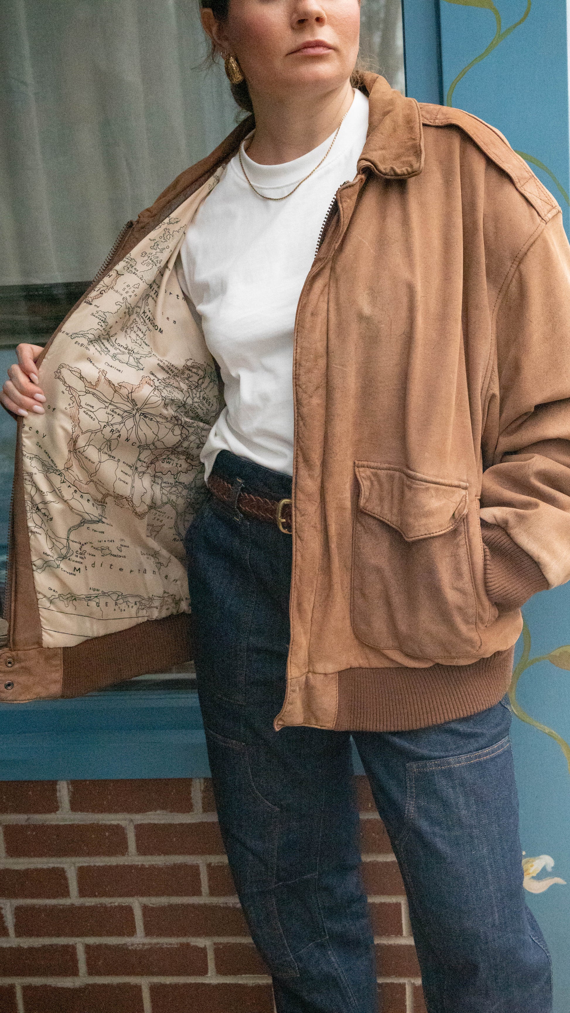 Woman stands in front of a vintage boutique in Chicago, Illinois wearing a leather jacket with a photo of a vintage map in the lining.
