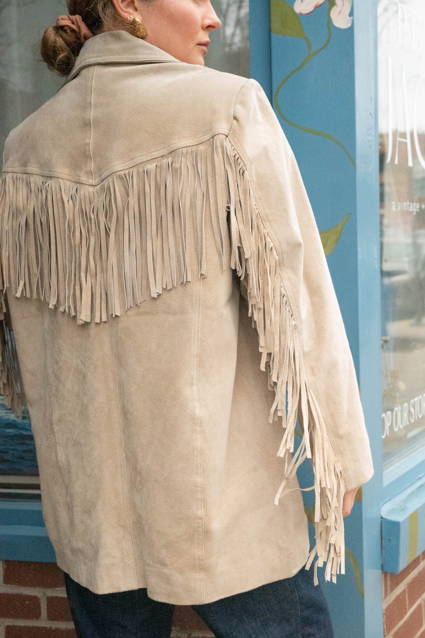 Boutique owner poses in vintage leather jacket with western fringe on the back