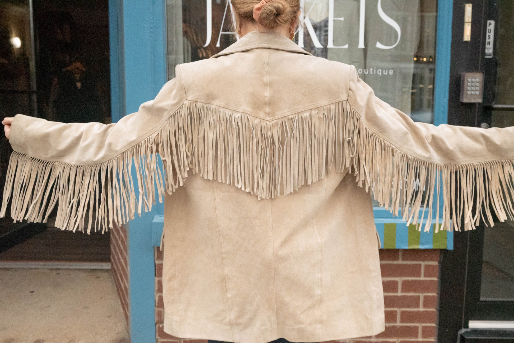 Woman holds her arms out to show off the fringe on her vintage leather jacket from local Chicago Vintage Boutique in West Town.