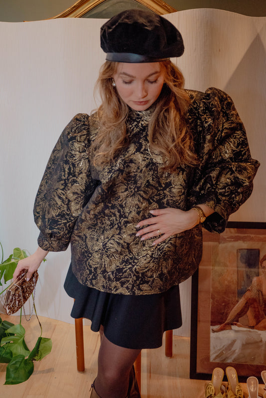 Woman wears a black beret with a gold and black regal vintage blouse posing for a dinner party themed styled vintage drop.