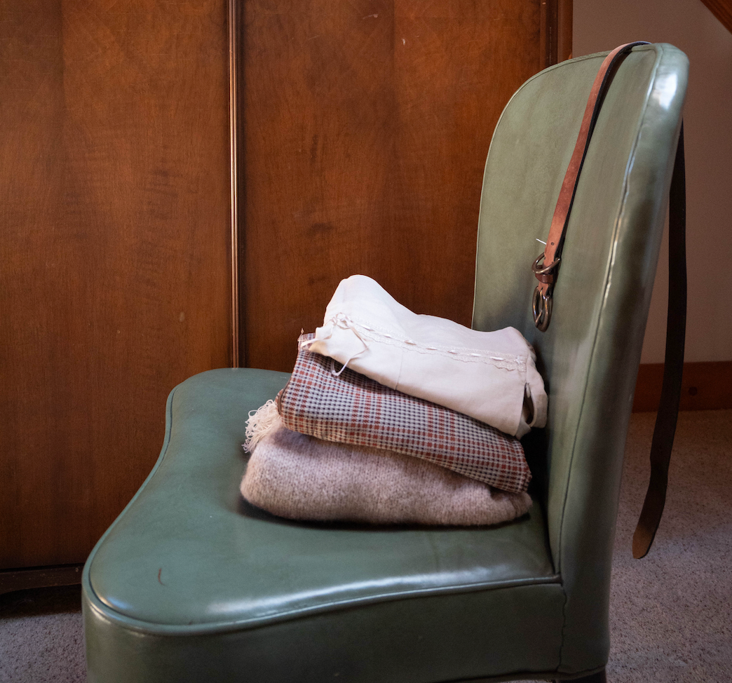 A teal chair sits in local Chicago Vintage Shop, Petals & Jackets with folded vintage sweaters and pants sitting on it.  Petals & Jacket's promotes sustainable shopping through local Chicago events like Clothing Swaps and workshops.