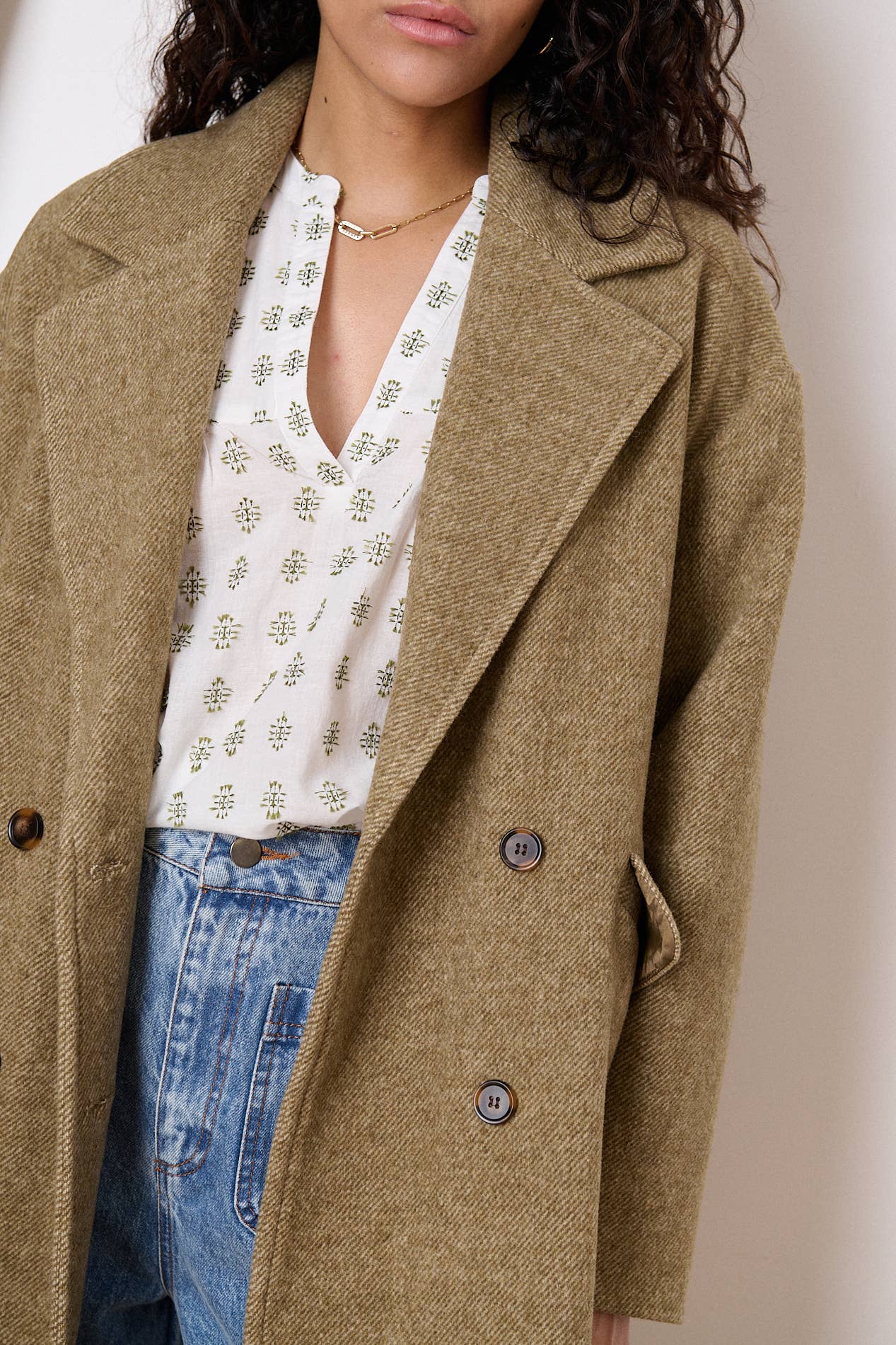 Young woman posing casually showcasing her camel colored wool winter coat paired with distressed denim jeans from local Chicago Modern and Vintage Boutique, Petals and Jackets. 