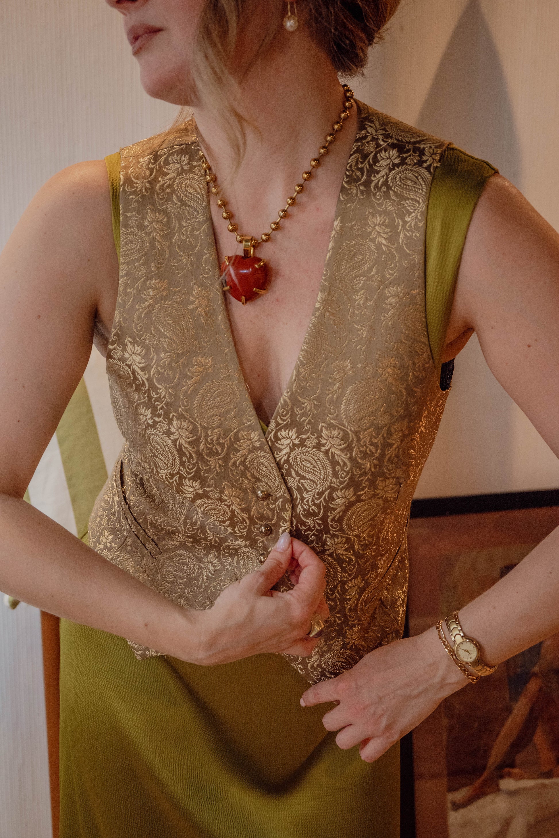 Petals and Jacket's boutique owner models a vintage green golden vest with gold detailing over an elegant green dress for a dinner party aesthetic. 