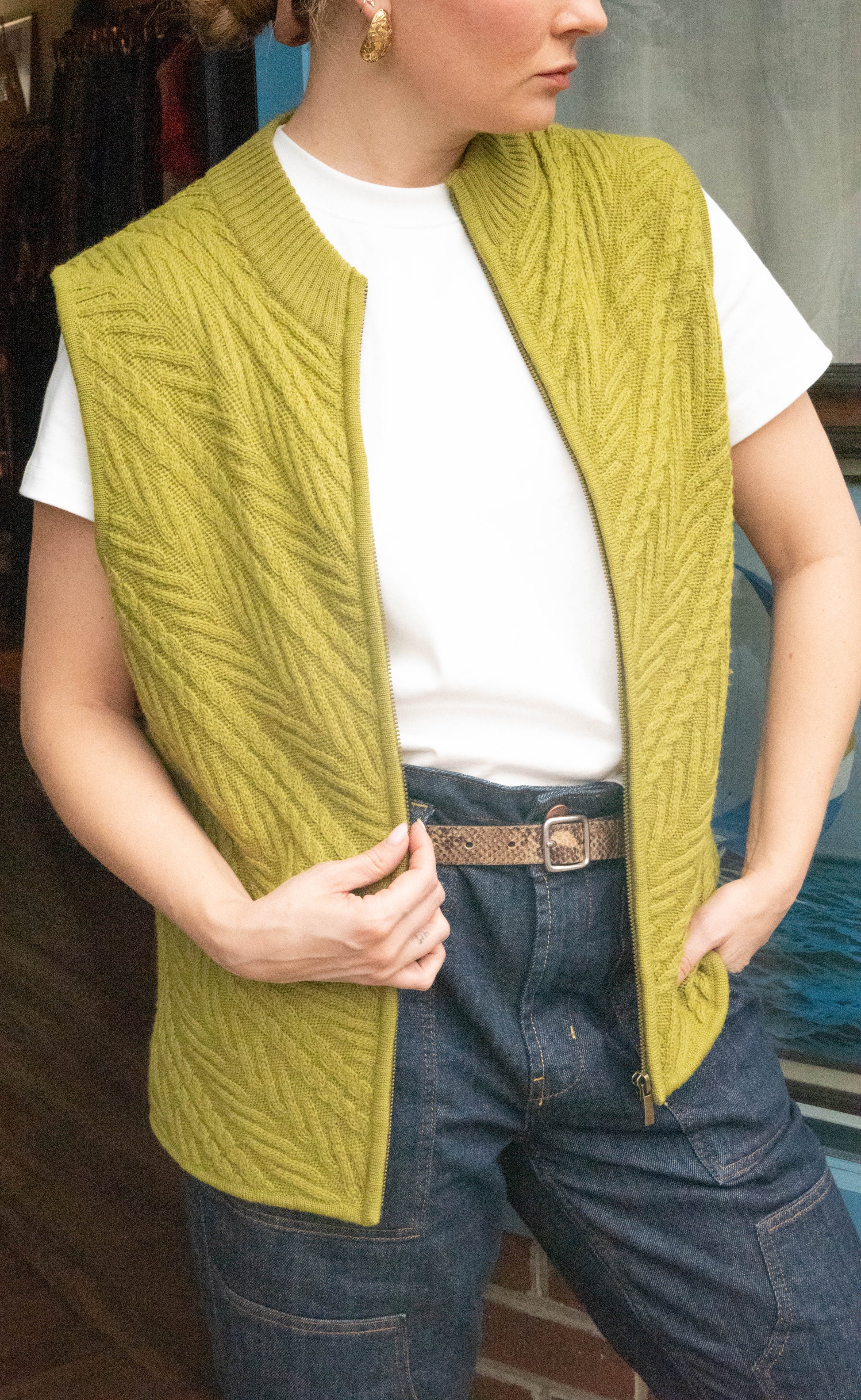 Woman stands in front of Petals and Jackets Vintage Shop in West Town Chicago Illinois wearing a vintage green vest from Coldwater Creek, denim oversized pants and a white shirt for her online vintage drops. 