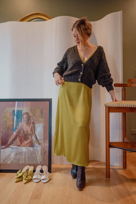 Woman wears a green dress with a black vintage sweater with gold detailing for a holiday themed shoot displaying new vintage items in her Chicago boutique Petals + Jackets. 