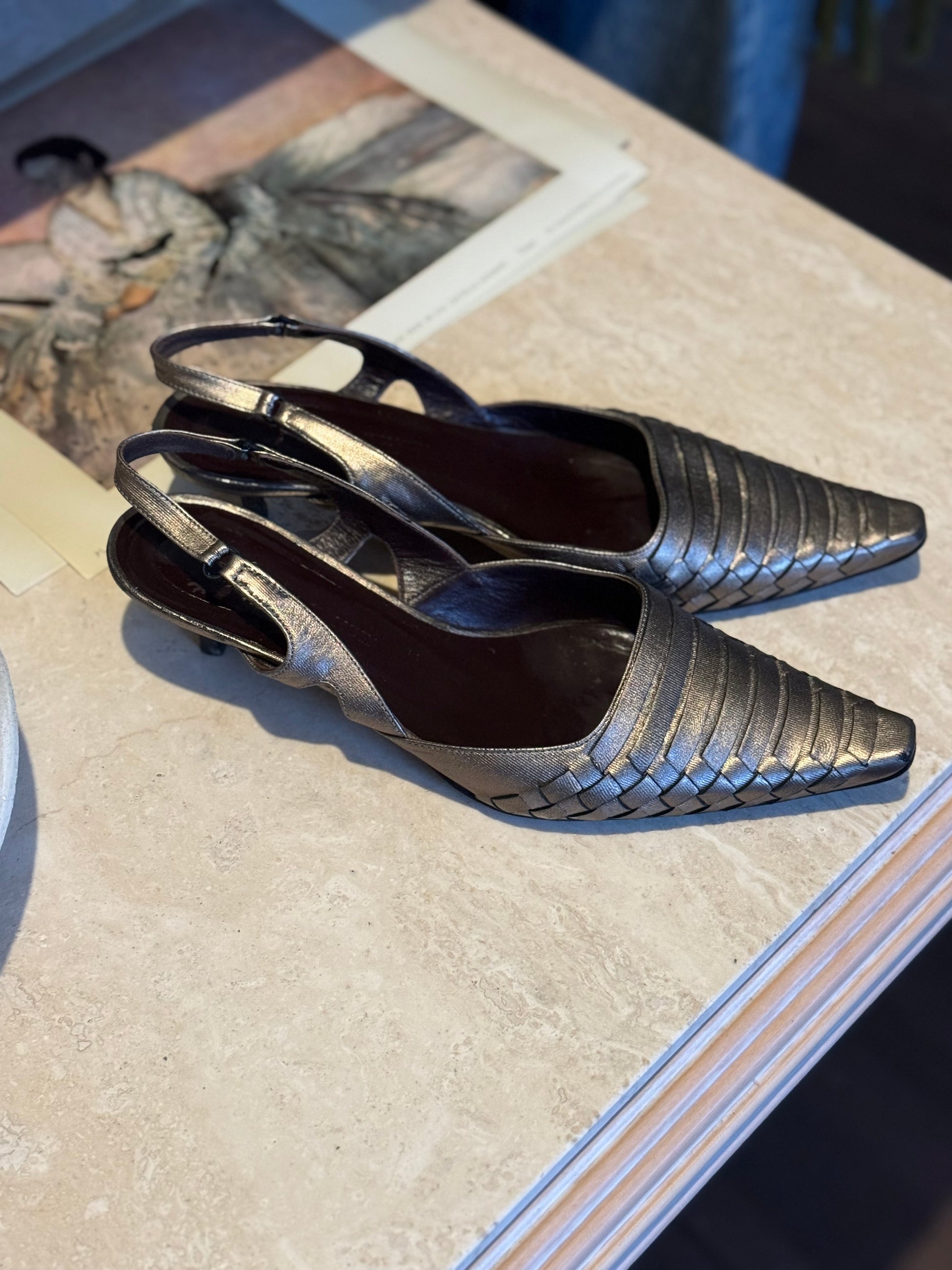 Vintage Bottega veneta metallic woven kitten heels sit on a marble table for display at local Chicago vintage shop Petals and Jackets. 
